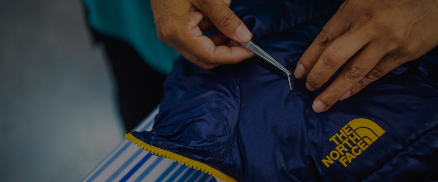 A close up of a factory worker’s hands as they repair a The North Face jacket for The North Face Renewed. 