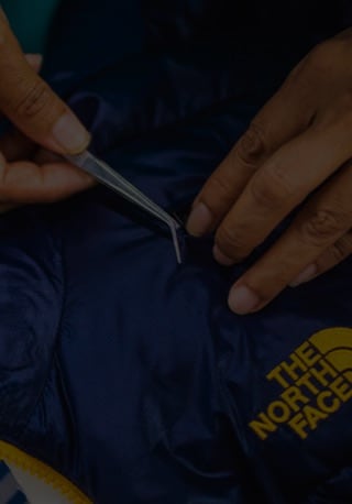 A close up of a factory worker’s hands as they repair a The North Face jacket for The North Face Renewed.