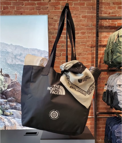A reusable bag from The North Face is on display in a retail store. A bandana, hat and thermos are peeking out.