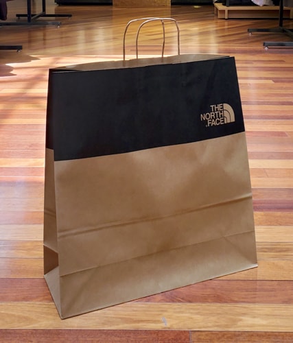 A FSC-certified paper bag from a The North Face retail store is displayed on a hardwood floor.