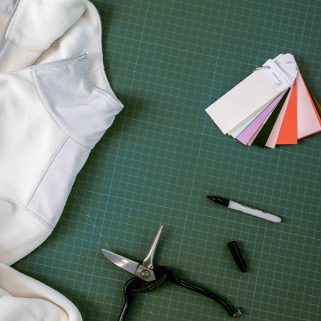 A circular fleece from The North Face rests on a sewing matt alongside color samples, scissors and a black marker.