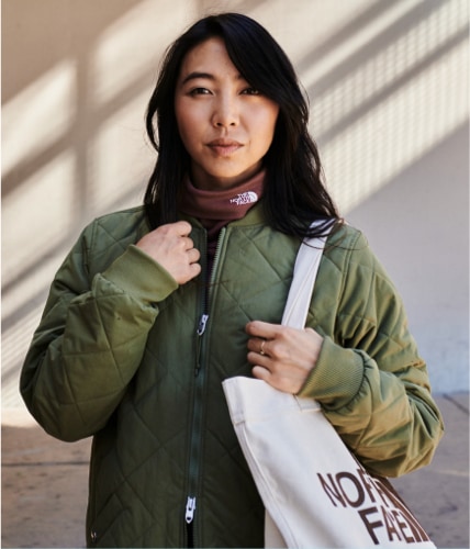 A woman wearing a green jacket is holding a reusable tote bag from The North Face.