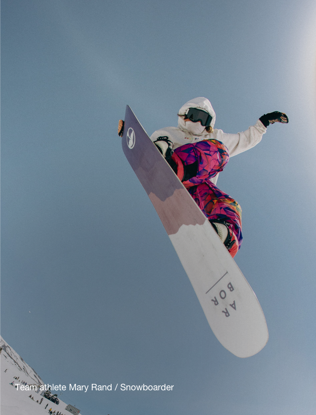 The North Face team athlete Mary Rand, wearing winter gear from the Pink Ribbon Collection, grabs her snowboard in the air.