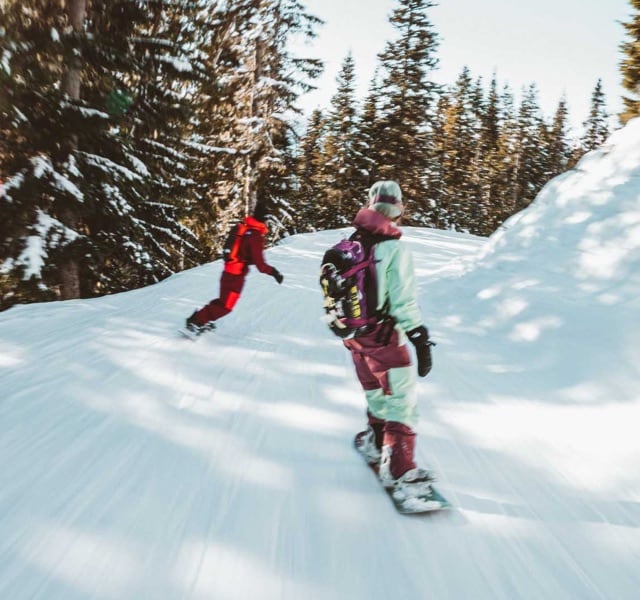 Two snowboarders riding on a cat track wearing the Freeride Collection from The North Face.