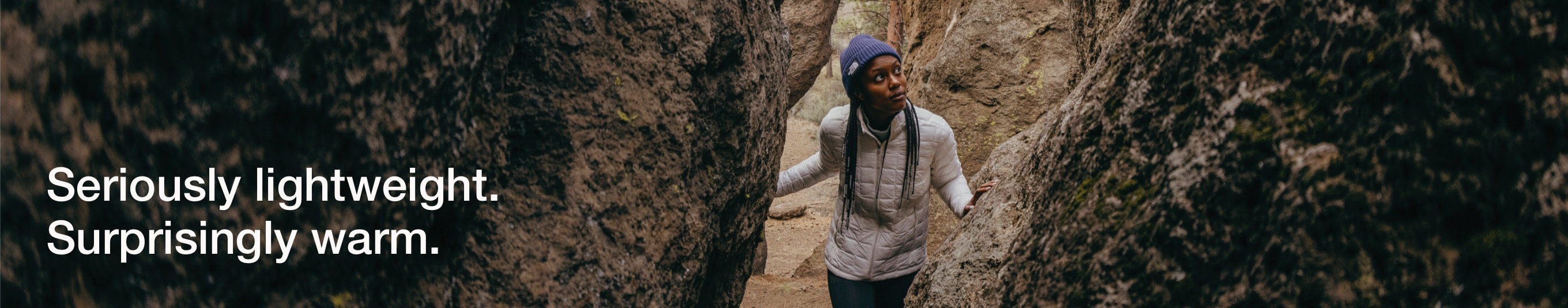 A hiker wearing ThermoBall™ walks between several large boulders. 