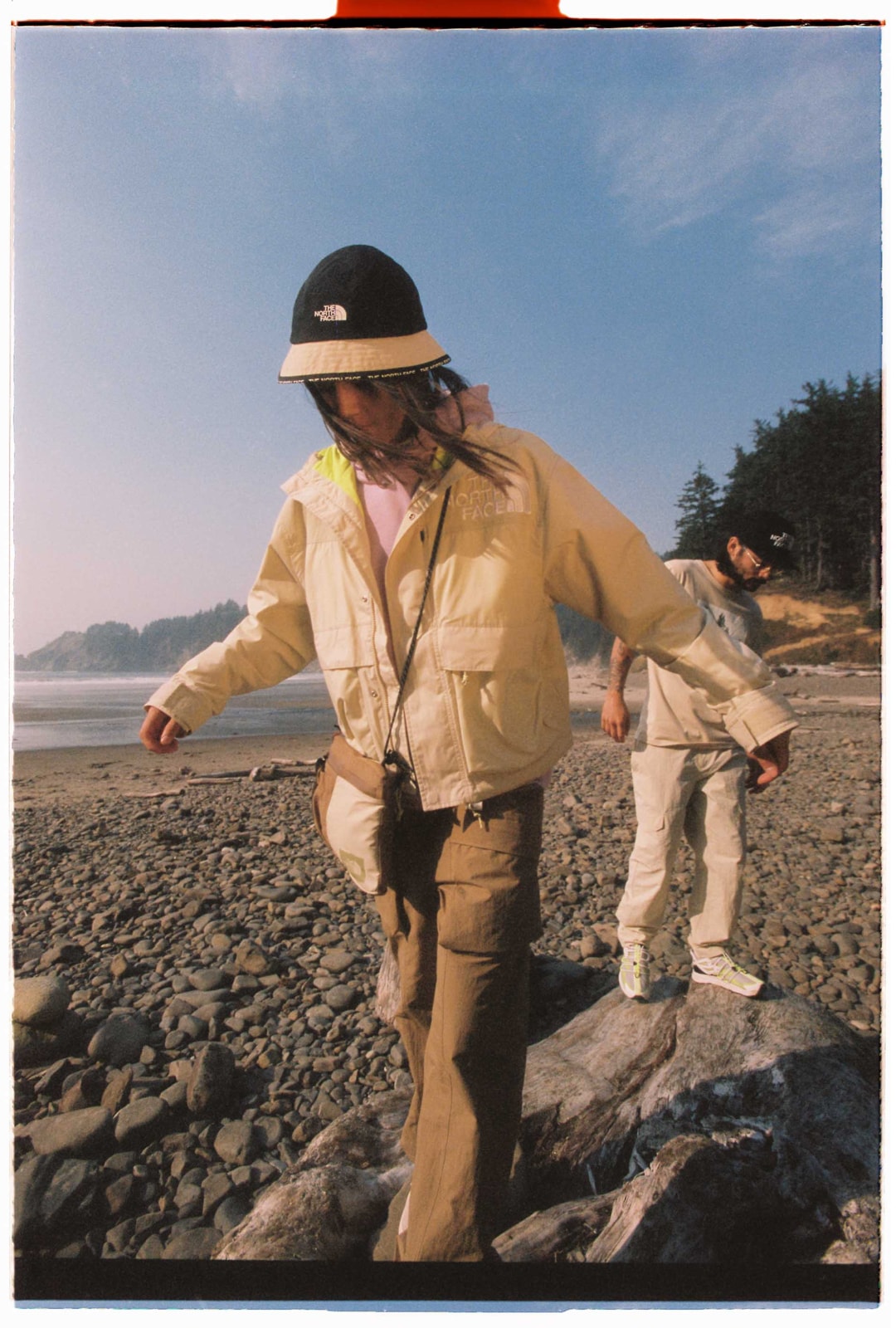 A person wearing the Women’s ’86 Low-Fi Hi-Tek Mountain Short Jacket walks across rocks on the beach.
