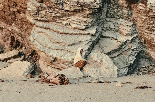 A person wearing the Low-Fi Hi-Tek Collection sits in front of a rocky cliff. 