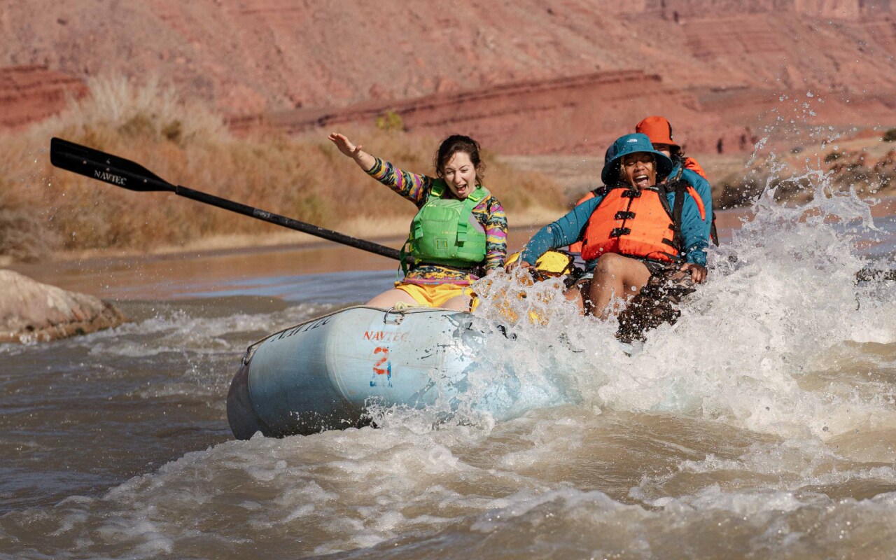 A group of rafters laugh as they splash through some rapids.