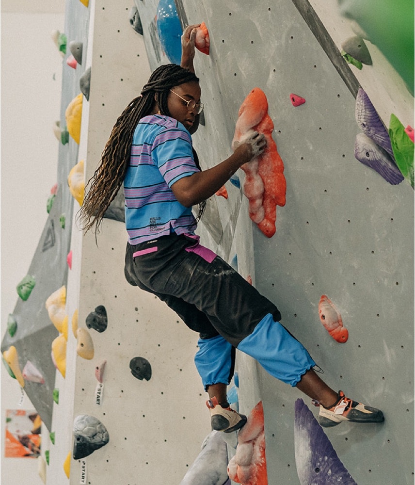 A rock climber wearing The North Face Black History Month collection contemplates their next move on an indoor wall.