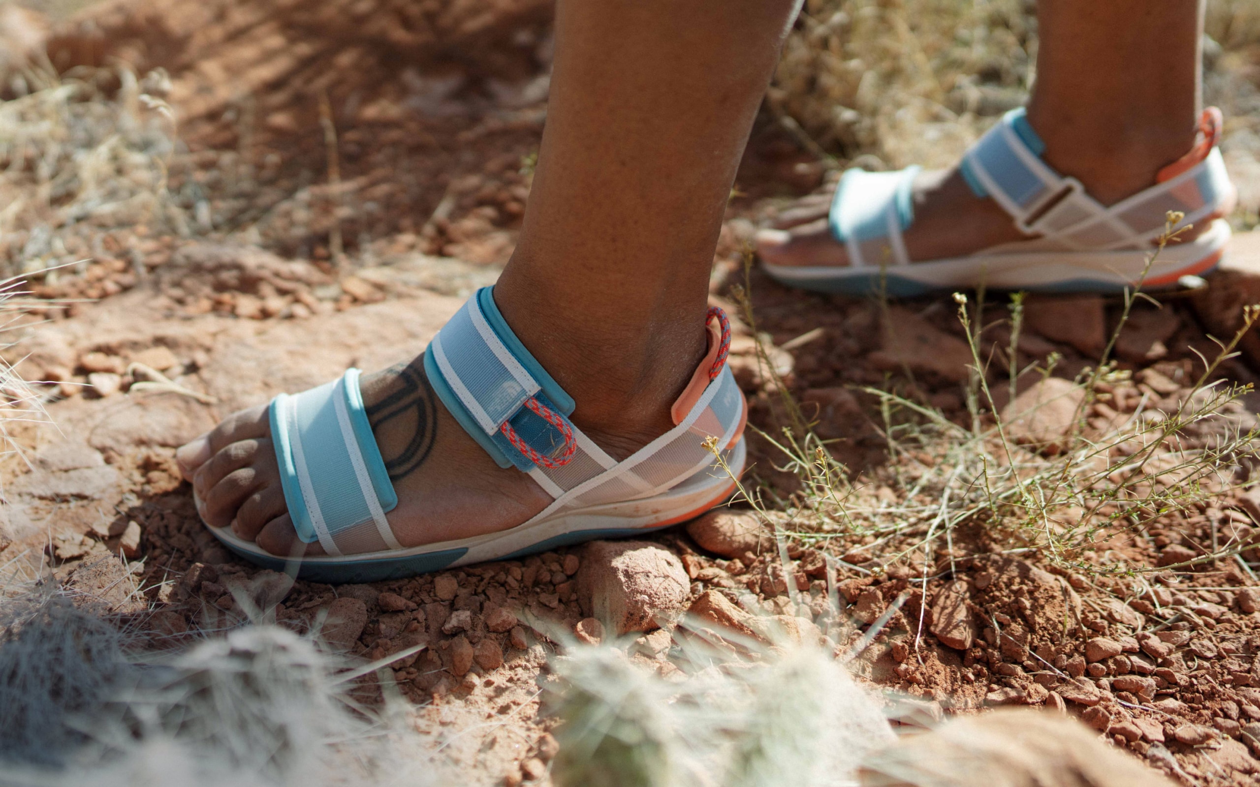 A close-up of a hiker walking through a desert landscape wearing sandals from The North Face.