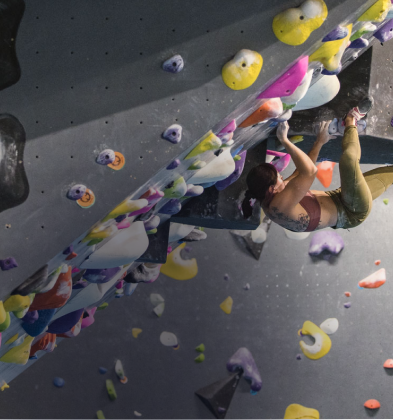A climber attempts to solve a bouldering problem while two friends wait below, ready to cushion any falls.