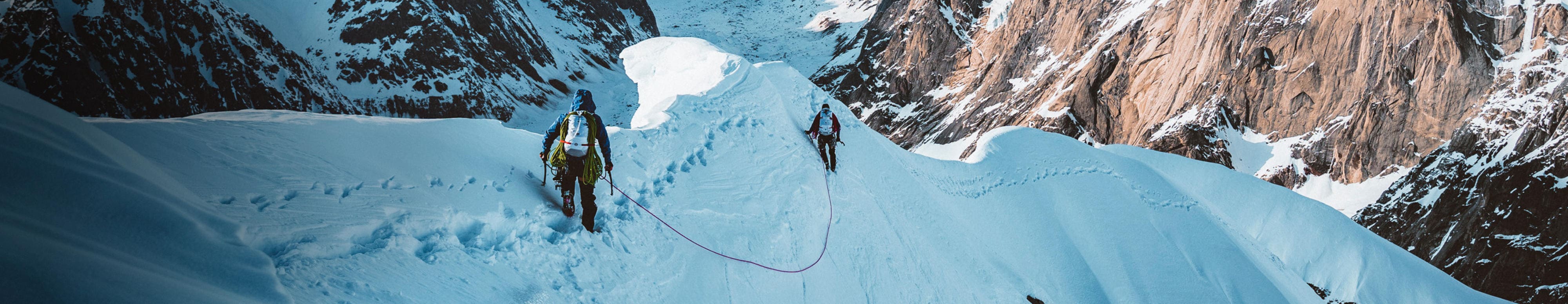 Two athletes use ropes to hike a mountain in the snow.