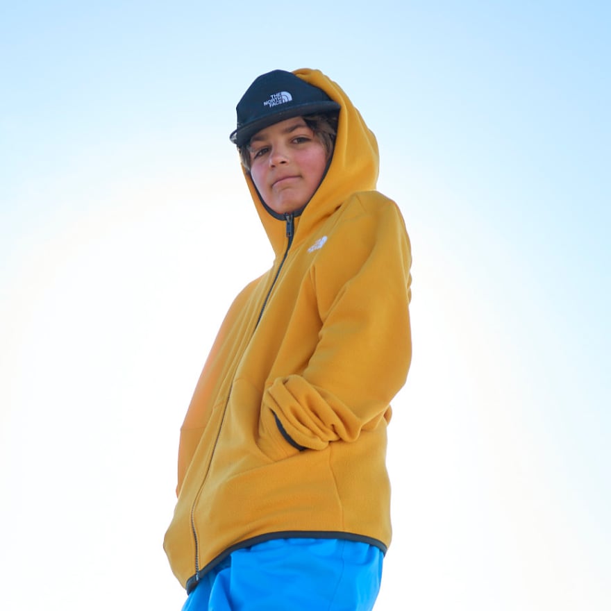 A child in a yellow hoodie stands against a blue sky.
