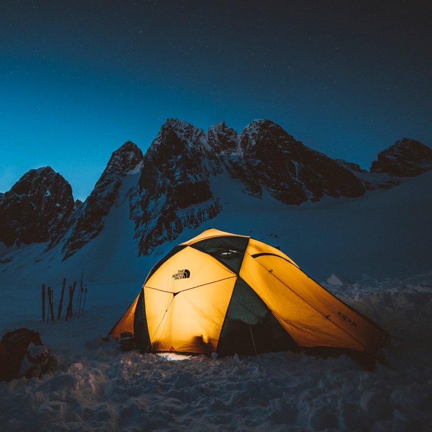 Une tente de The North Face, illuminée de l’intérieur, sur fond de ciel sombre et montagneux.