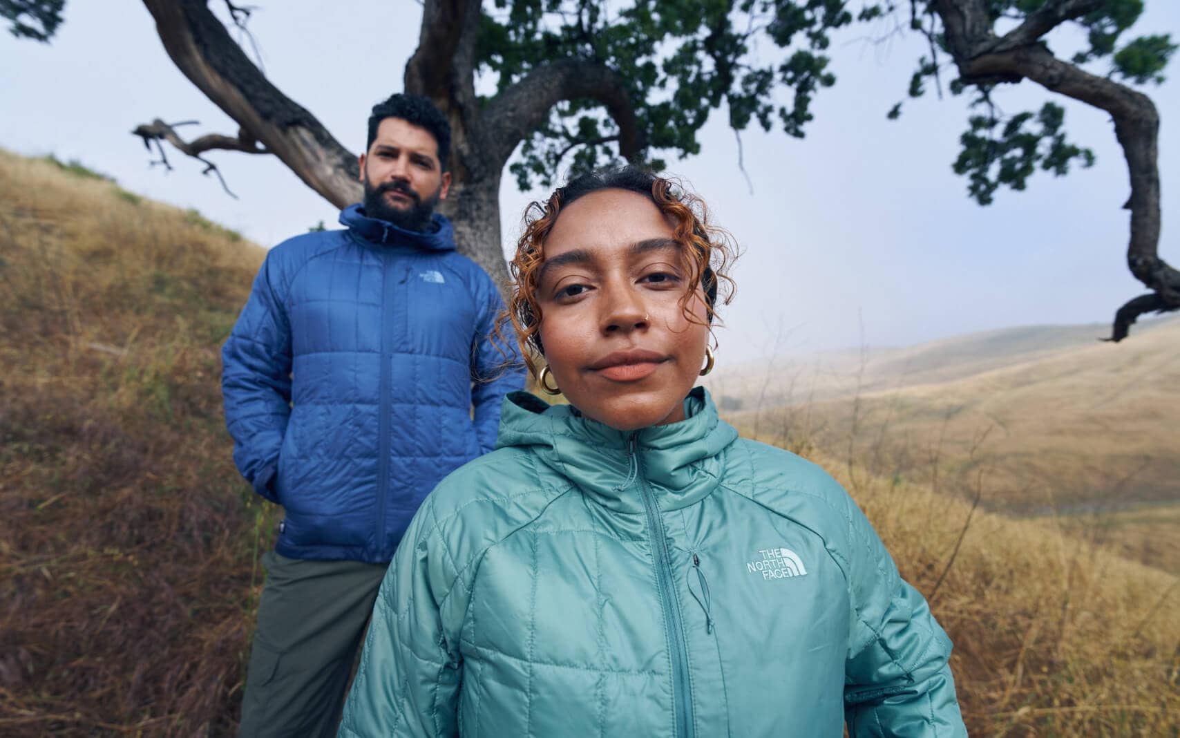 Two people wearing Circaloft Jackets from The North Face are hiking through a field of grass.