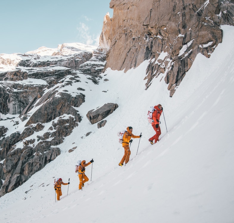 A team of athletes in a line climbs to the peak of a snowy mountain in gear from The North Face.