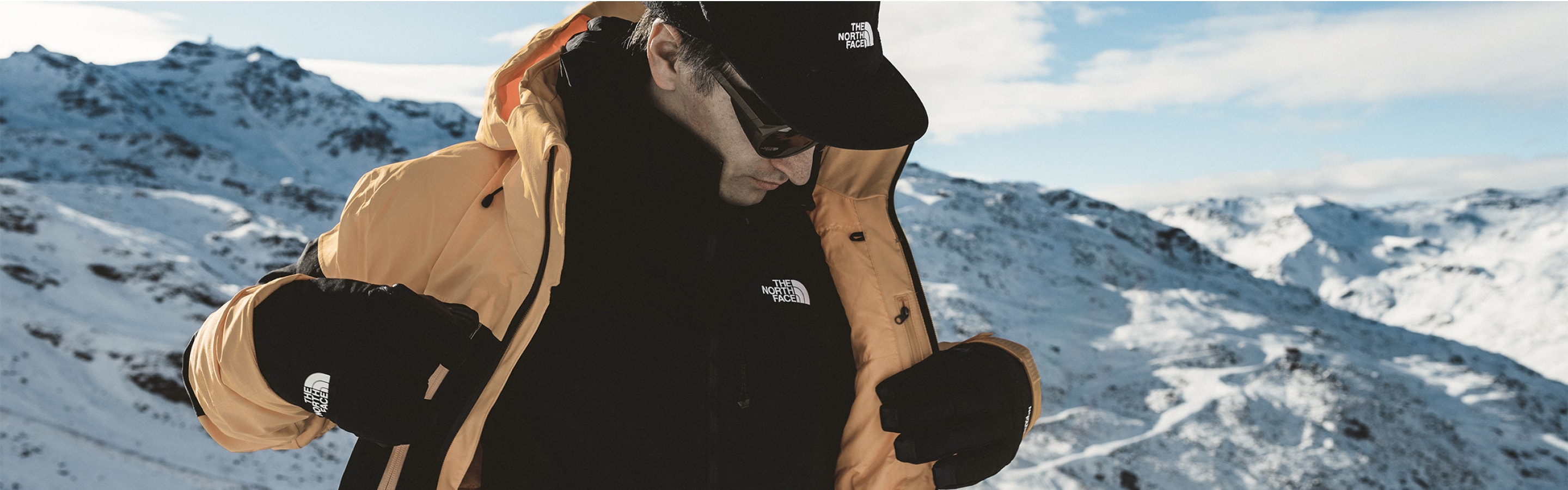 Une personne se tient debout sur un sommet de montagne enneigé et porte un assortiment de vêtements HeatseekerMC Eco.