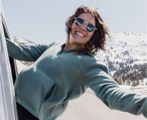 Person smiling while hanging outside of car with mountains in the background.