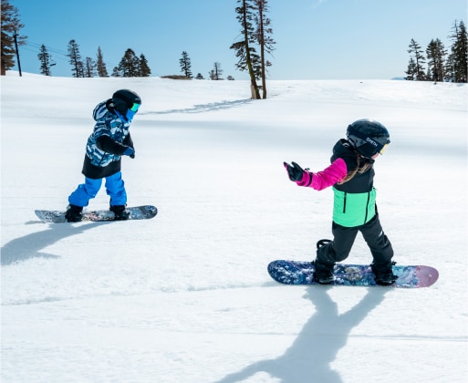 Two children snowboarding down a slope.