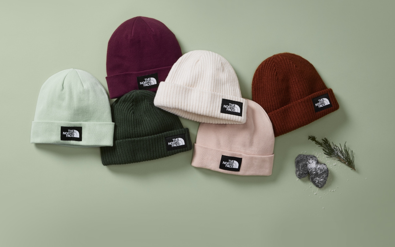 An overhead view of six beanies in multiple colors laid out on a green background. 