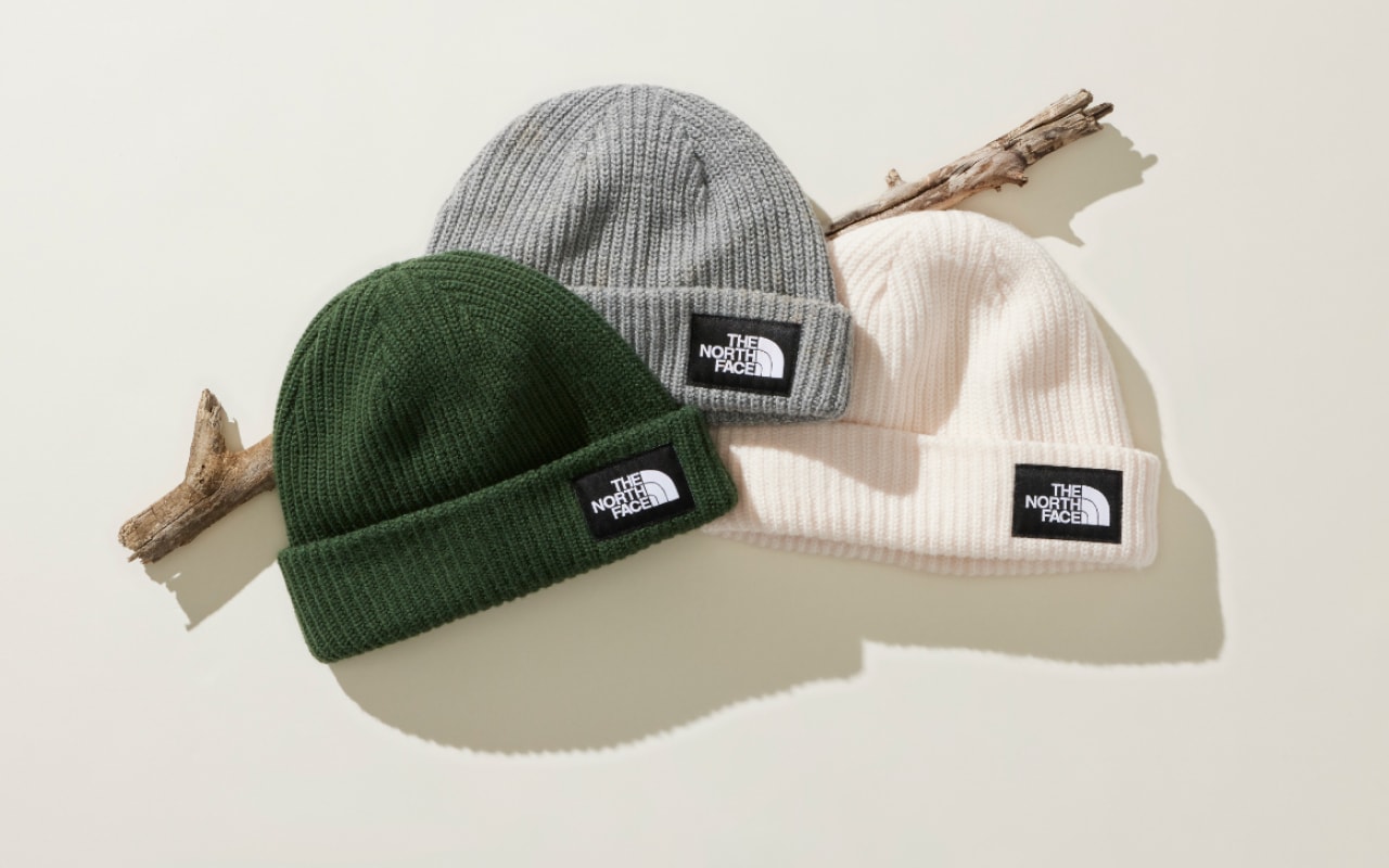An overhead view of green, grey and white beanies laid out on a white background. 
