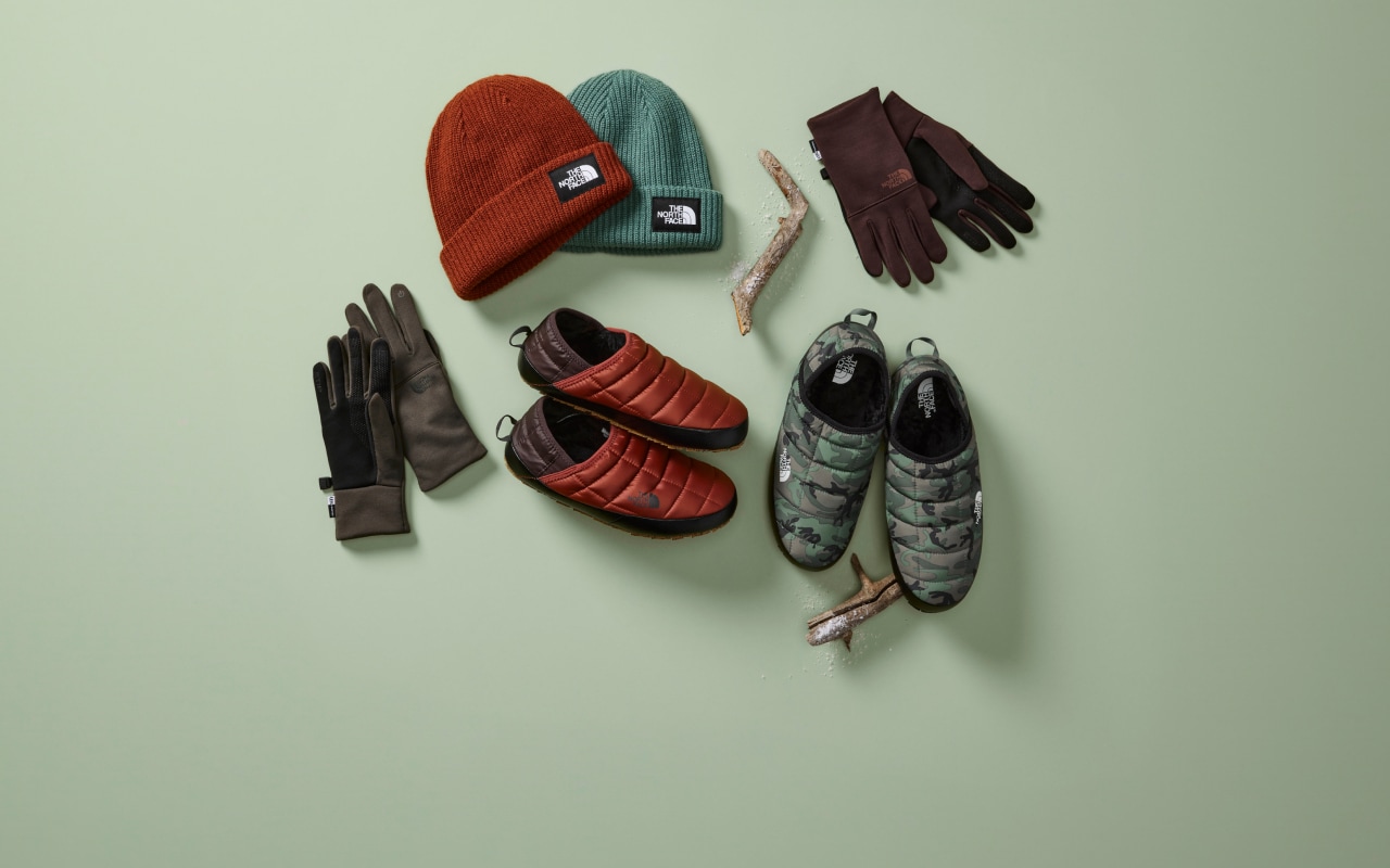 An overhead view of gloves and slippers laid out on a green background.