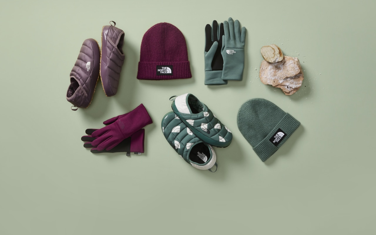 An overhead view of gloves, slippers and a beanie laid out on a green background. 