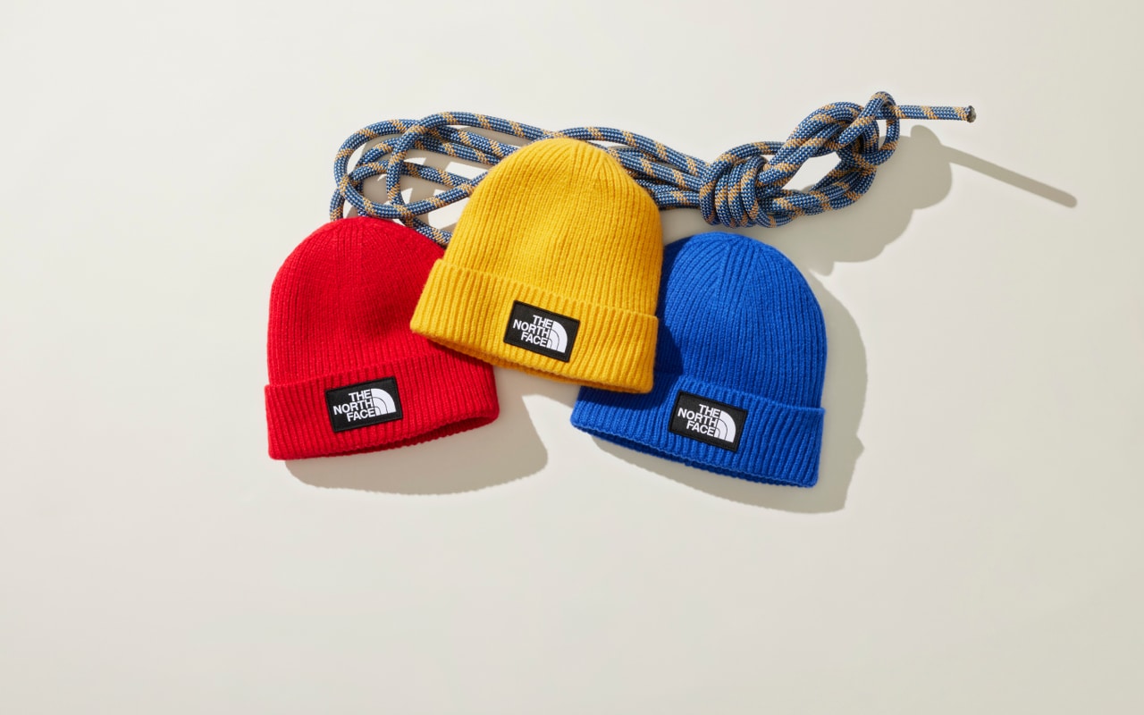 An overhead view of red, yellow and blue beanies laid out on a white background next to climbing rope.