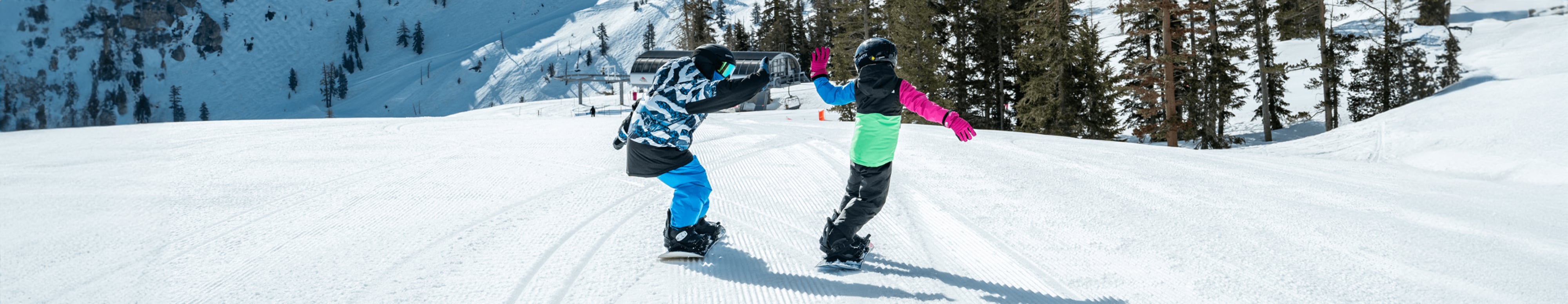 Two kids high-five while snowboarding down the slopes of a mountain resort. 
