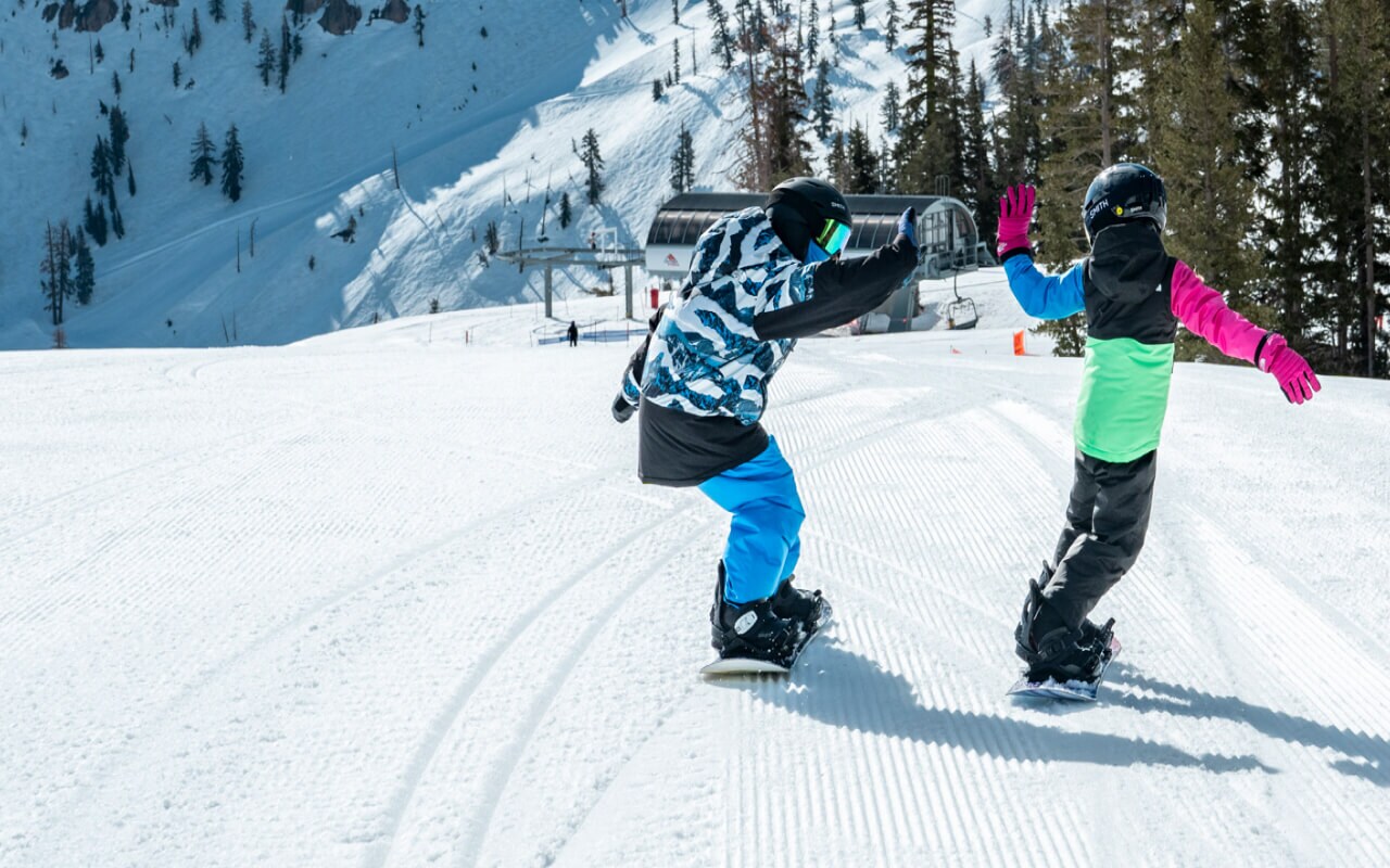 Two kids high-five while snowboarding down the slopes of a mountain resort. 