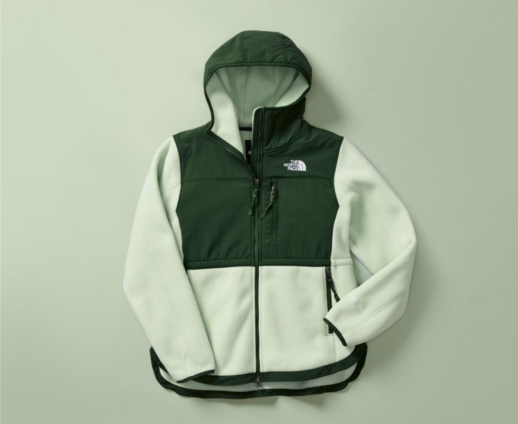 A laydown of the women’s Denali Jacket on a green background. 
