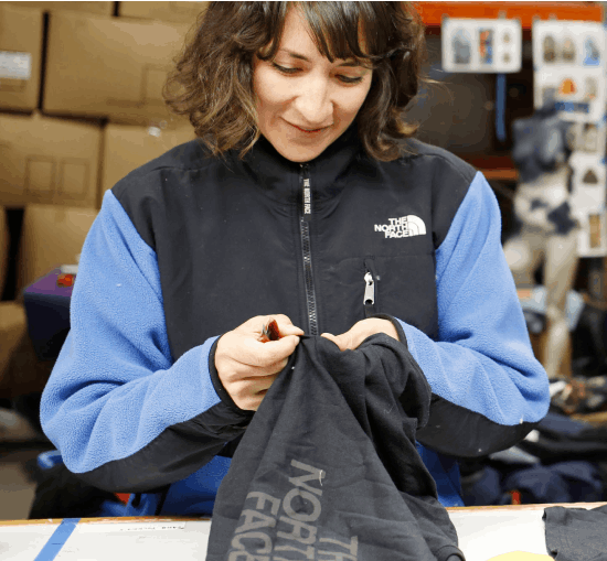 A woman in a repair shop stitches a jacket from The North Face for their Renewed program.