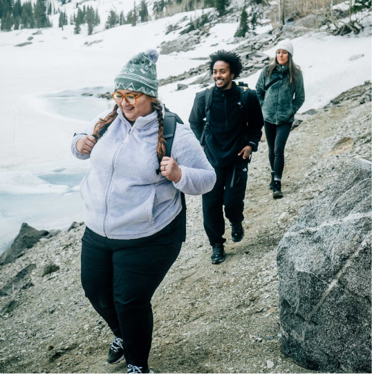 Trois amis, deux femmes et un homme, portant des vêtements de la marque The North Face marchent sur un sentier enneigé.