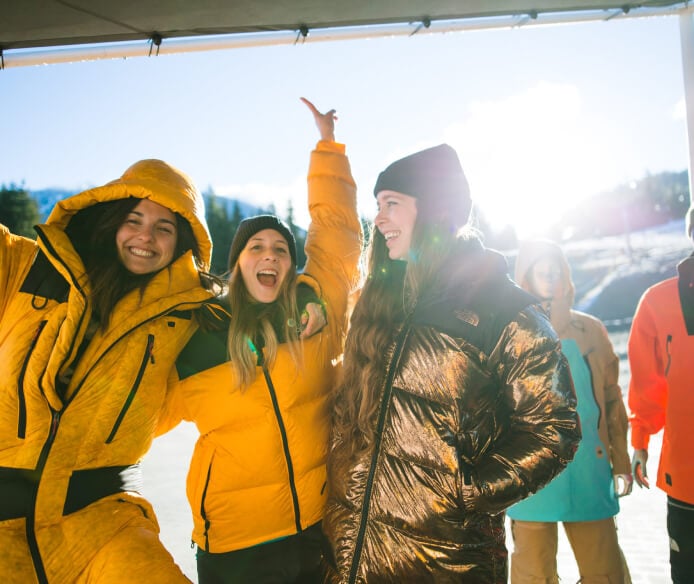 Trois personnes souriantes portent des articles de la gamme hiver 2023 de The North Face.