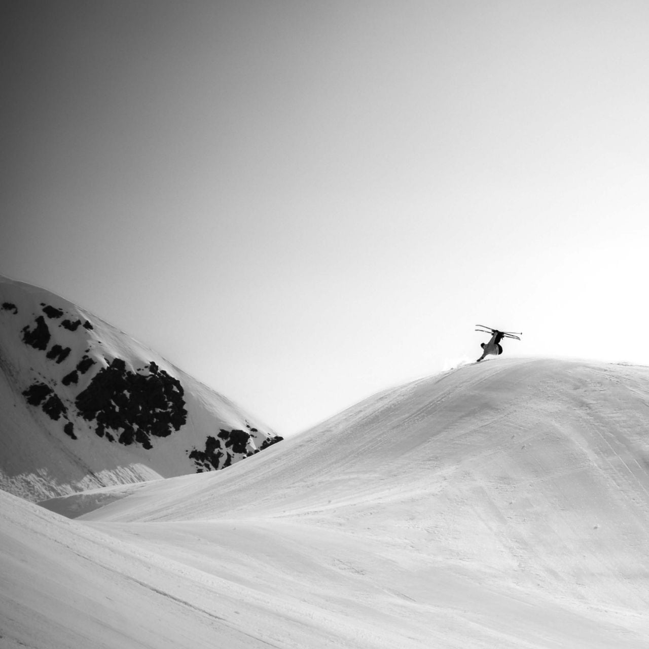 Image en action de l’athlète The North Face Dennis Ranalter effectuant une figure à skis sur une colline enneigée et damée. 