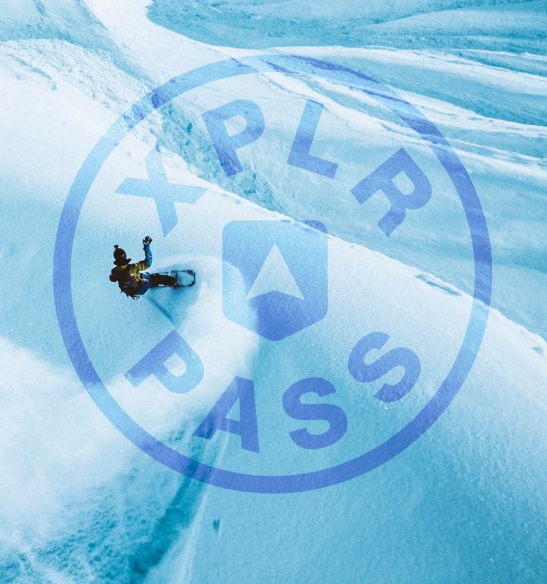 A snowboarder carves down a mountain tinged blue beneath a superimposed XPLR Pass logo. 