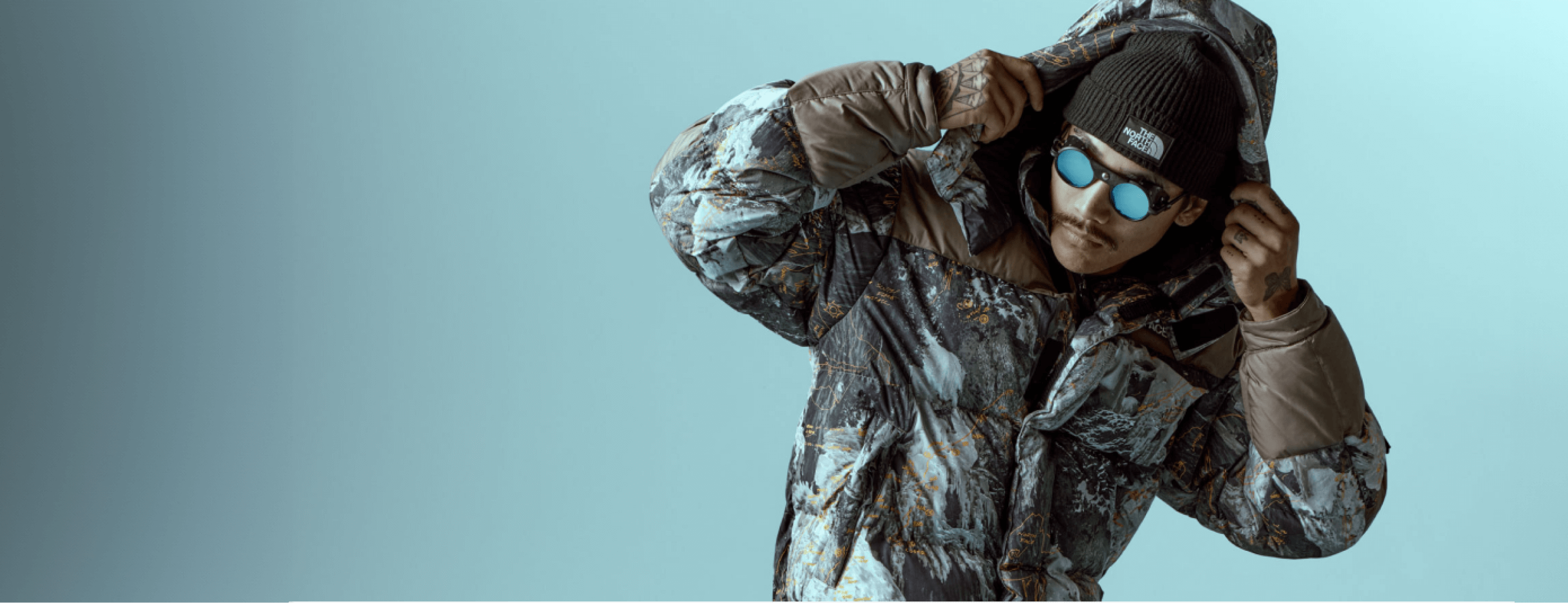 A person wearing the HMLYN Baltoro Jacket from Conrad Anker’s Notes Collection adjusts the hood in front of a blue background. 