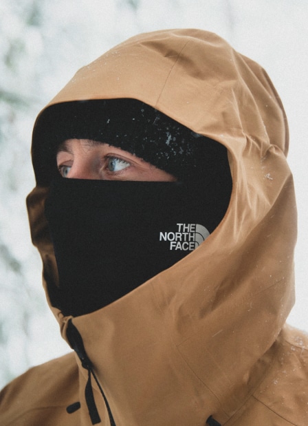 Man wearing neck gaiter over his face with a hooded The North Face jacket.