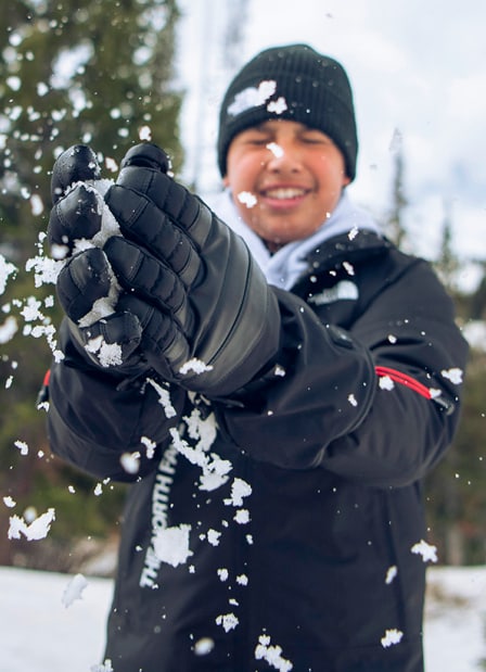 Kid wearing The North Face beanie while holding snow and smiling.