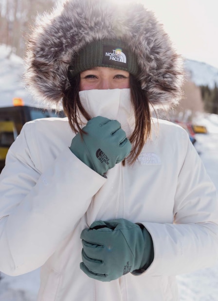 Woman wearing a white parka with green The North Face beanie.