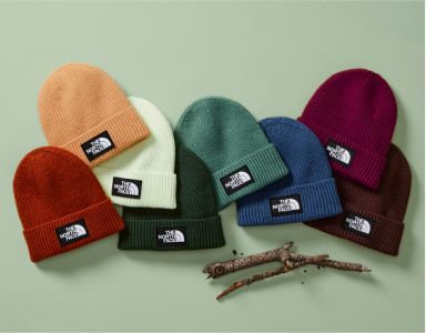 An overhead view of beanies in multiple colors laid out on a green background. 