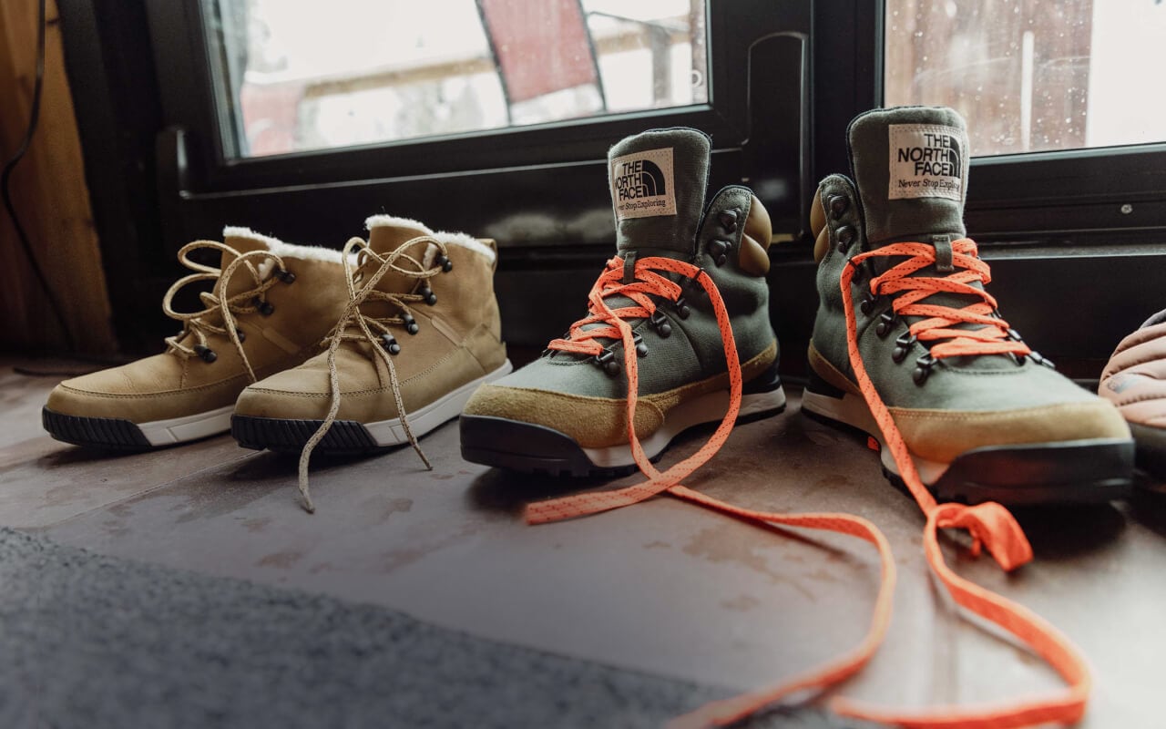 Inside a cabin, by the door, sit two different pairs of winter boots from The North Face.