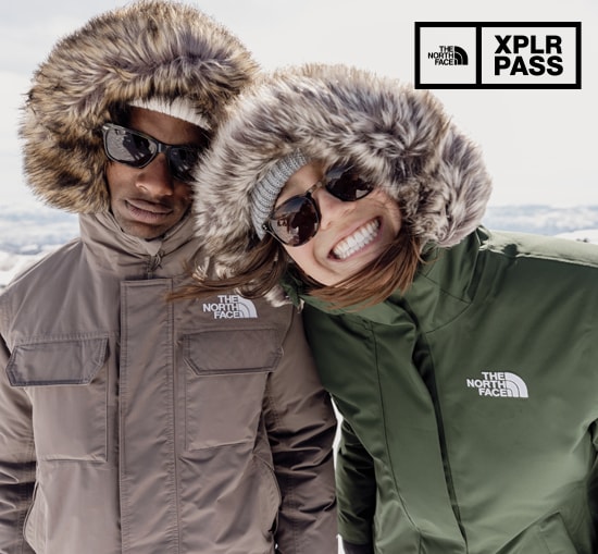 A man and a woman smile for the camera in faux- fur hooded parkas from The North Face.