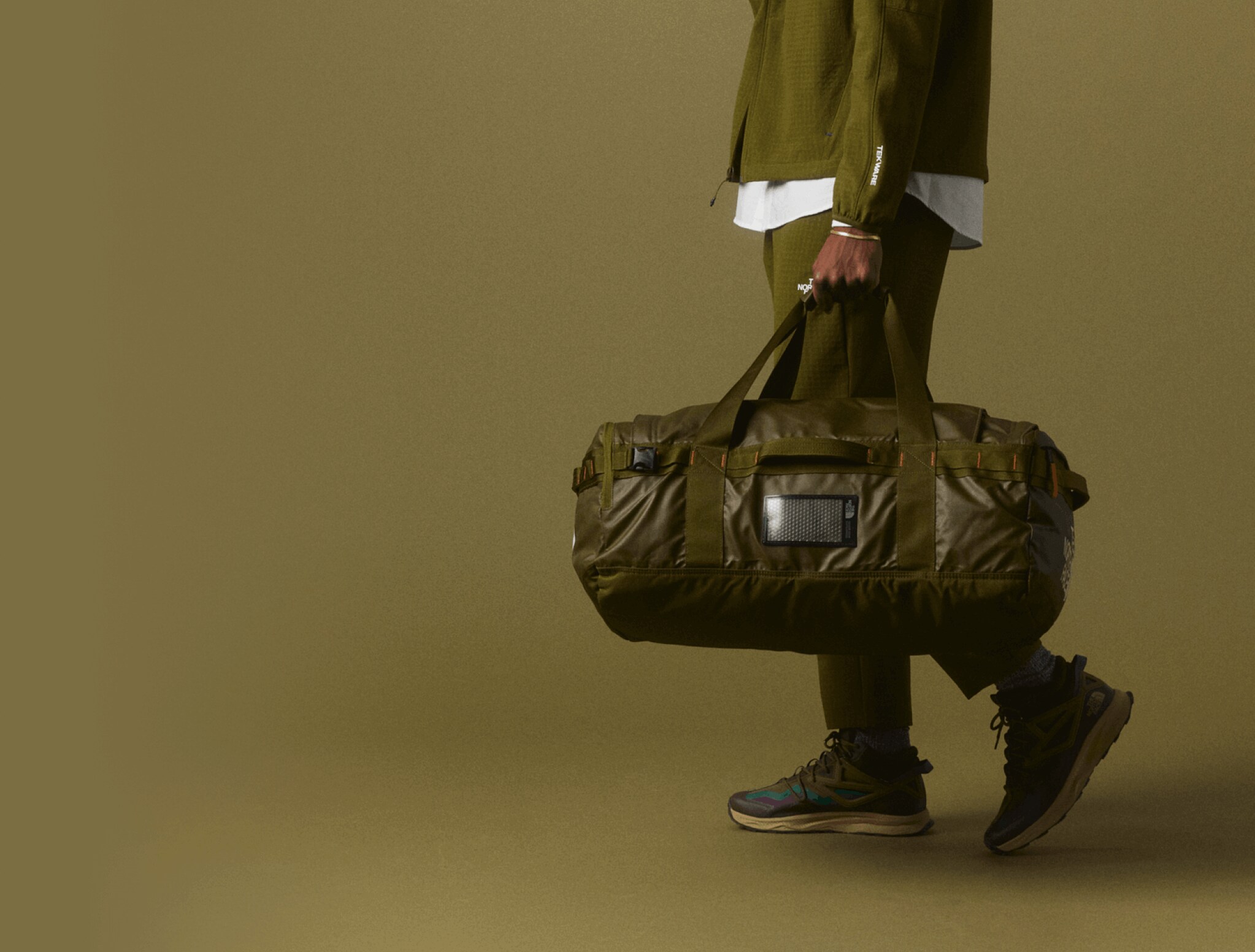 Studio shot of tonal olive green outfit and Base Camp Voyager Duffel on olive background.