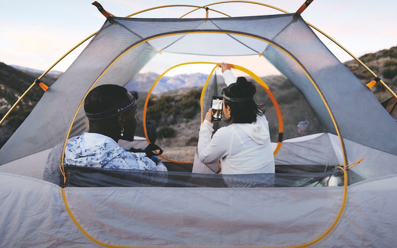 Two people are in a tent from The North Face with the rain fly off. One person is taking a photo of the mountainous view with their phone. Text reads: “All the space you need—for all the views you want.” 