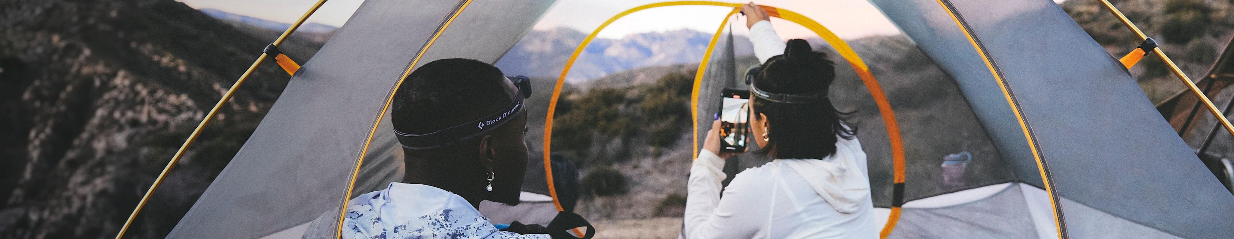 Two people are in a tent from The North Face with the rain fly off. One person is taking a photo of the mountainous view with their phone. Text reads: “All the space you need—for all the views you want.” 