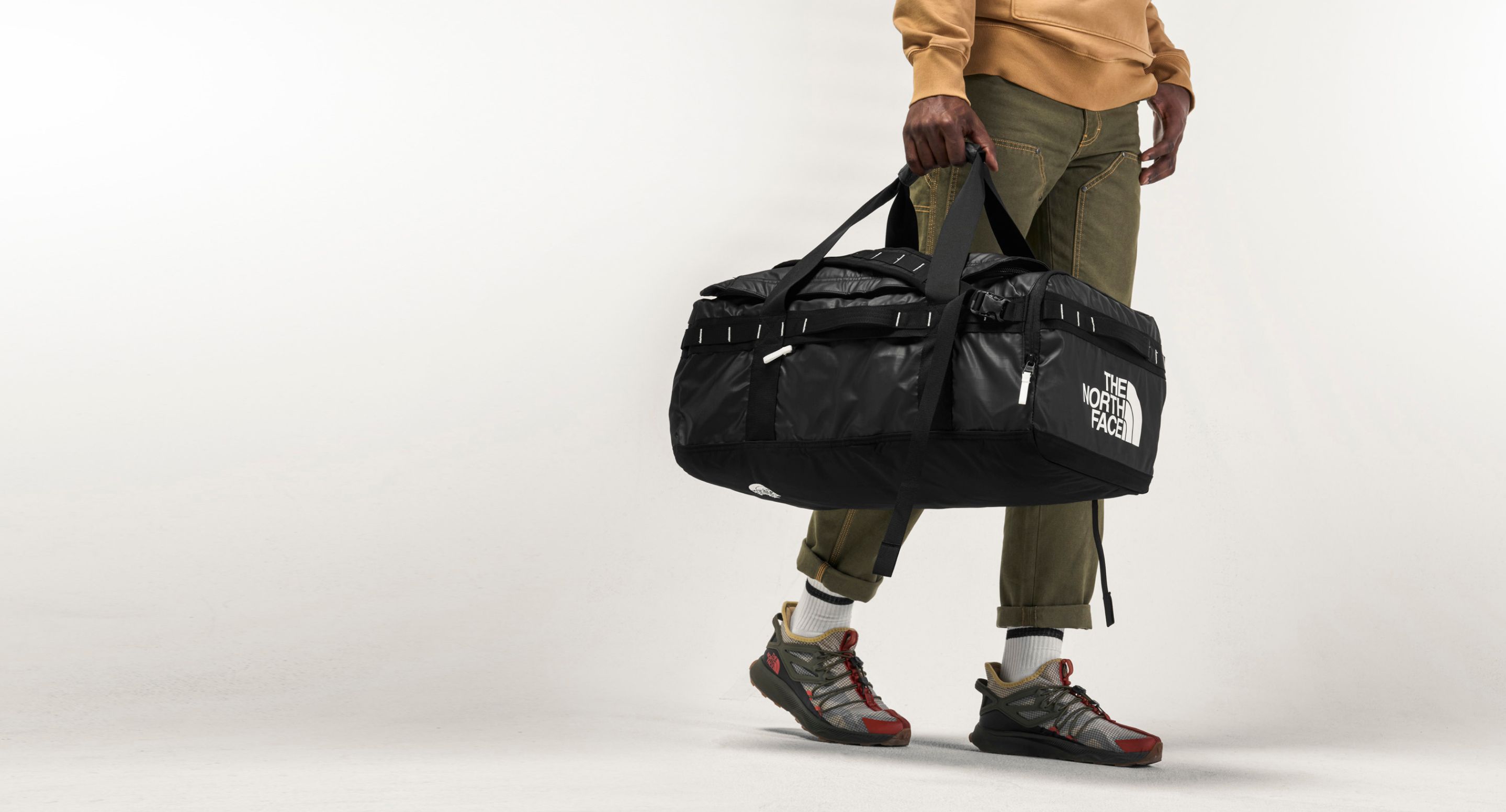  A person carrying the Base Camp Voyager Duffel by The North Face. Text reads: “You’re going places.” 