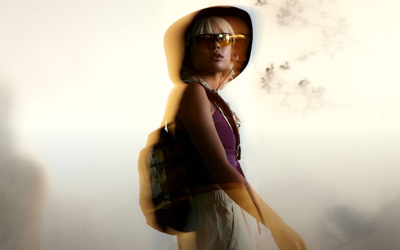 A person is wearing a sun hat, protective glasses, and a tank top. The background is blurred. Text reads: “Discover new arrivals.” 