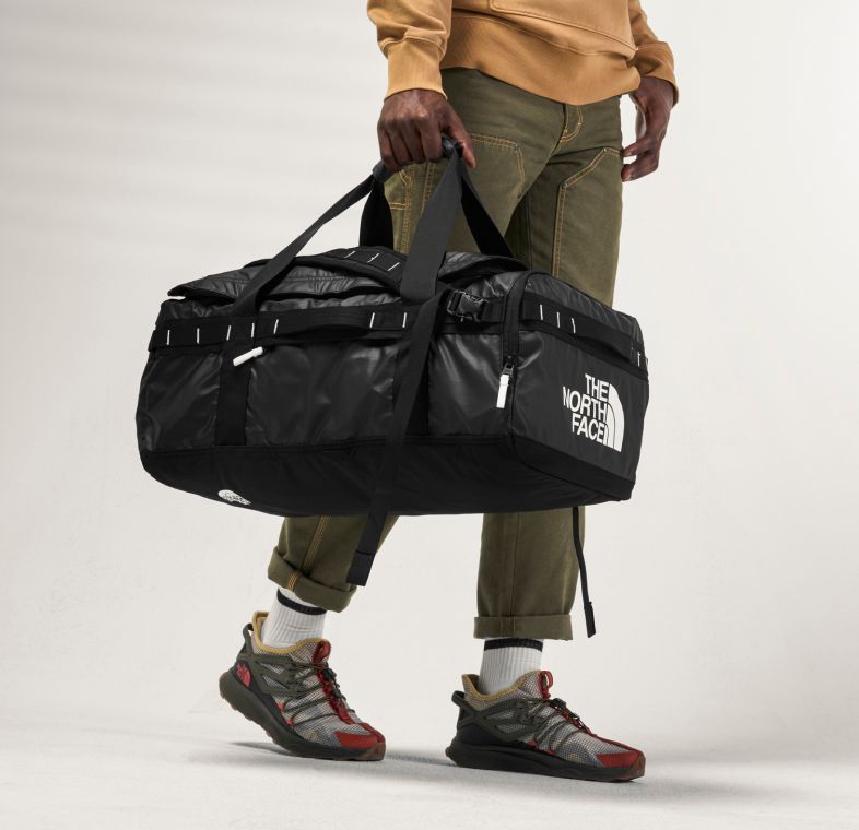  A person carrying the Base Camp Voyager Duffel by The North Face. Text reads: “You’re going places.” 