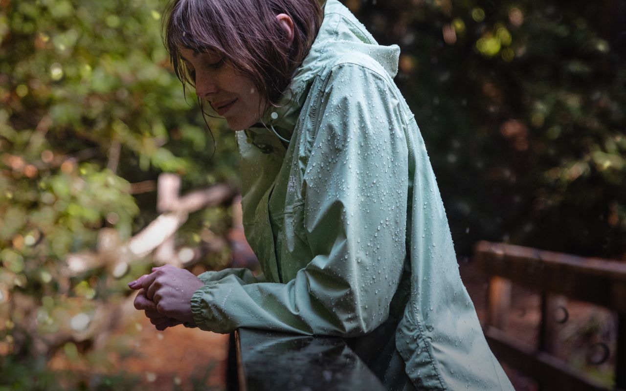 A close-up shot of a person hiking in the rain. They’re smiling, wearing a rain jacket from The North Face. Text reads: Focus on everything but the forecast.” 